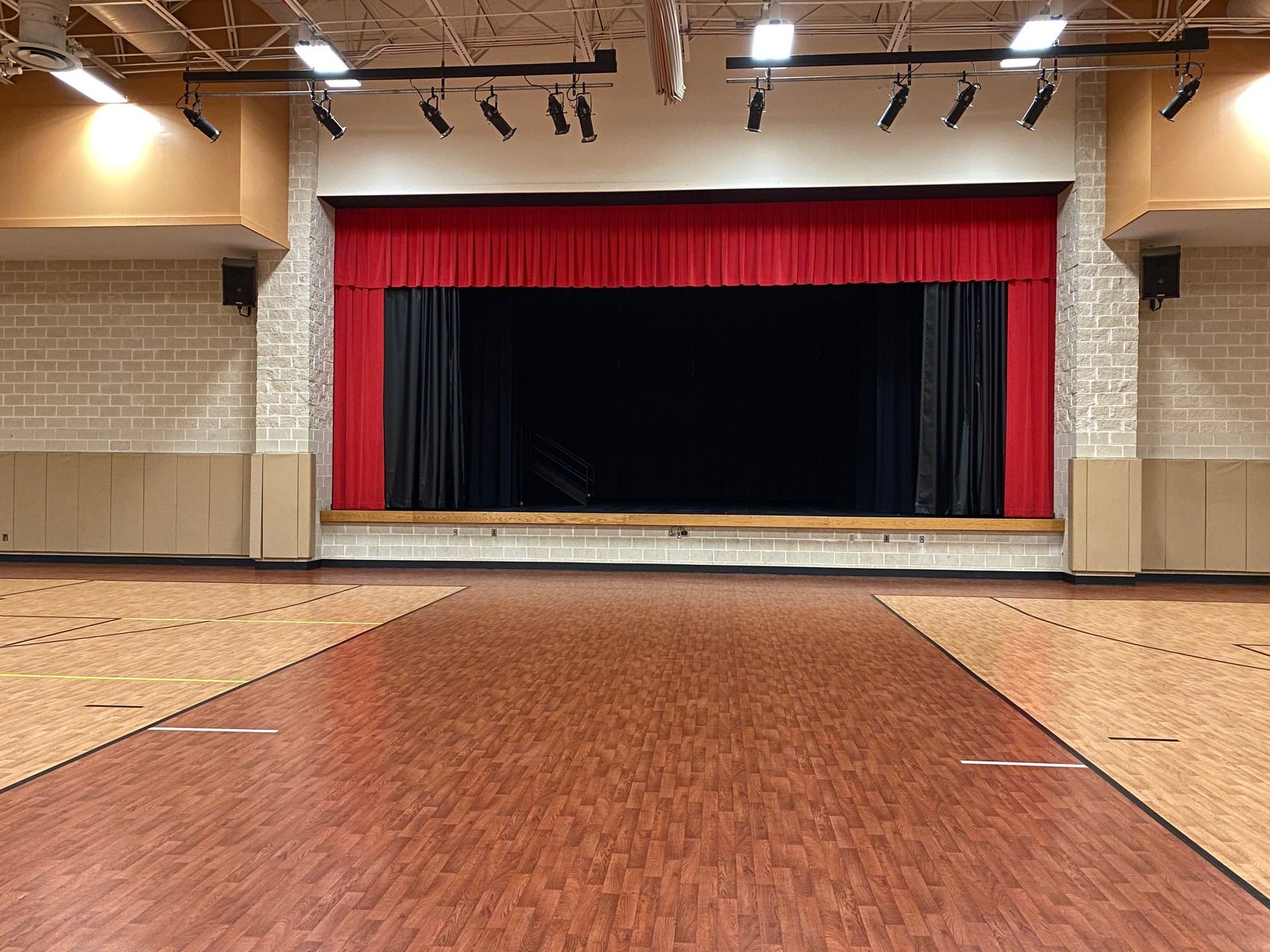 Gym floor facing the stage with red curtains at the Mebane Arts & Community Center